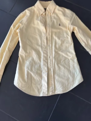  långärmad skjorta från Polo Ralph Lauren - Säljer en klassisk skjorta från Polo Ralph Lauren med broderad logga på bröstet. Skjortan har lång ärm, knappar hela vägen och en snygg krage. Perfekt för dig som gillar stilrena plagg och vill ha något som funkar till många outfits.