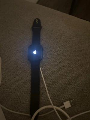 Apple Watch med svart silikonband - Smartklocka från Apple med svart silikonband och rektangulär skärm. Klockan har en stilren design och laddas med medföljande USB-kabel. Perfekt för dig som vill ha koll på notiser, träning och hälsa direkt på handleden.