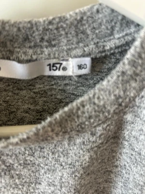 Grå puffärm tröja från 157 - Säljer en grå tröja från 157 med puffade korta ärmar och rund halsringning. Materialet är mjukt och stickat, perfekt för dig som gillar en enkel men trendig look. Passar dig som vill ha något stilrent och comfy.