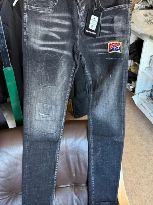 Svarta Dsquared2 jeans med patch - Coola svarta jeans från Dsquared2 med slitningar och en färgglad patch med texten 'DSQ2 1964' på framsidan. Jeansen har en slim fit och är tillverkade i denim med snygga detaljer och tvättad look. Perfekt för dig som vill sticka ut.