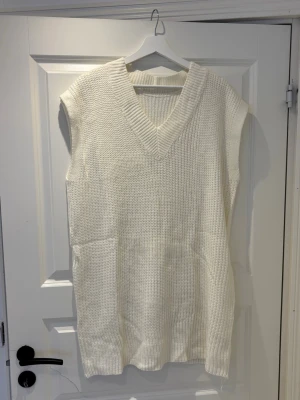 Vit stickad väst med v-ringning - Säljer en stilren vit stickad väst med bred v-ringning och ribbade kanter. Västen är ärmlös och har en relaxed passform som passar perfekt över en skjorta eller t-shirt. Enkel att matcha och ett måste i garderoben för en trendig lager-på-lager-look.