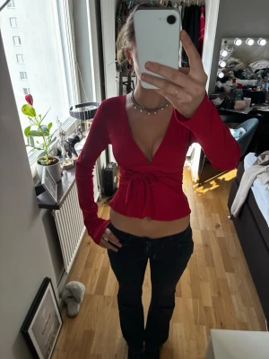 Röd topp från Nelly - Säljer en snygg röd omlottopp från Nelly i ribbad bomull. Toppen har djup v-ringning, långa ärmar och knytband i midjan som ger en croppad look. Perfekt för dig som vill ha något trendigt och bekvämt.