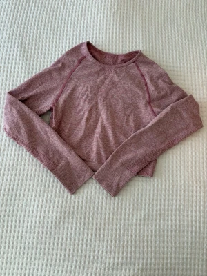 Rosa croppad långärmad topp - Säljer en croppad långärmad topp i ljusrosa nyans. Toppen har rund halsringning, tumhål i ärmsluten och är tillverkad i ett mjukt, stretchigt syntetmaterial. Perfekt för dig som gillar en sportig och bekväm stil.