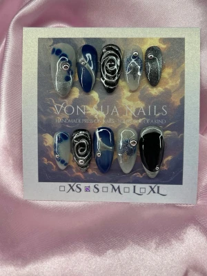 BlueMirage (S);Medium Almond - Unika Handgjorda press-on naglar i en medium lång mandelform. Setet har en mix av blå, svart, silver och vita nyanser med swirl-mönster, glitter och små dekorativa stenar. Storlek i  S: 15 mm, 11,5 mm, 12 mm, 11 mm, 9 mm , och designen är unik med både cateye och 3D handmålade detaljer.