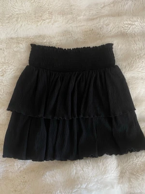 Svart volangkjol - Svart ribbad volangkjol från Kappahl i storlek 146/152 men passar mig som brukar ha xs. Bra skick.