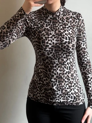 Leopardmönstrad långärmad polotopp - Säljer en slim långärmad polotopp med leopardmönster i bruna, svarta och beige toner från New Yorker i strl XS. Toppens material är troligtvis polyester och den har en hög krage som ger en cool look. Perfekt för dig som gillar djurmönster och vill sticka ut.