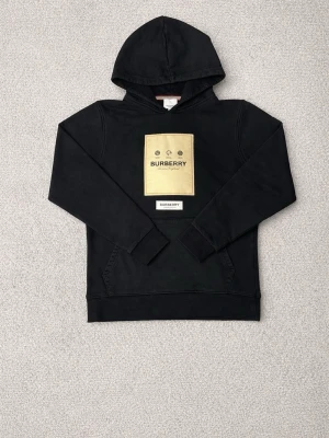 Svart hoodie från Burberry med logga - Svart hoodie från Burberry med stor beige logga framtill och klassisk huva. Storlek M men skulle säga att den är mer S 