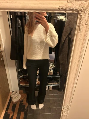 Svarta kostymbyxor med utsvängda ben - Säljer ett par svarta kostymbyxor med utsvängda ben och låg midja. Byxorna har en klassisk passform och är sydda i ett slätt tyg som ger en stilren look. Perfekta att matcha med en stickad tröja eller skjorta.