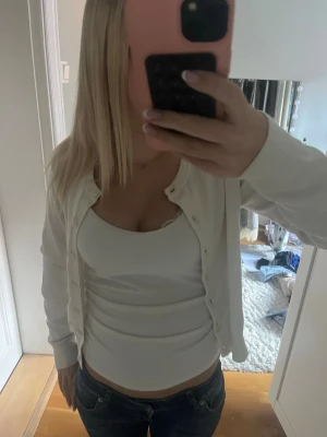 Vit basic kofta med rund hals - Säljer en enkel och stilren vit kofta med rund hals och knäppning framtill. Koftan har långa ärmar och en smal passform som passar perfekt till jeans eller kjol. Materialet känns mjukt och stretchigt, vilket gör den bekväm att bära hela dagen.