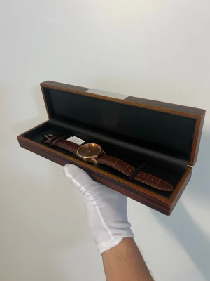 Limited edition one made - Guld Cosmos klocka med läderband - One made only. Hand assembled. Stilren klocka från Cosmos med ett guldigt ur och brunt läderband med krokodilstruktur. Klockan har minimalistisk design utan siffror och levereras i en elegant träbox. Perfekt för dig som gillar klassiska accessoarer med modern touch.