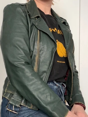 Mörkgrön skinnjacka, S - Cool mörkgrön skinnjacka med klassisk bikerstil, sneddragna dragkedjor och fickor med metallknappar.