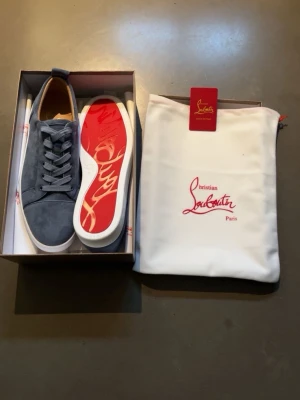 Baby blue Christian Louboutin  - Snygga blåa sneakers från Christian Louboutin med klassisk röd sula och signaturmönster. Skorna är tillverkade i mocka med vita kanter och har en låg profil. Perfekt för dig som vill sticka ut med exklusiva detaljer och stilren design.