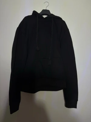 Svart hoodie med graffiti-tryck - Svart hoodie med stor ficka framtill och justerbara snören i huvan. På huvan finns ett coolt graffiti-inspirerat tryck i vitt och grått. Hoodien har en avslappnad passform och ribbade muddar vid ärmar och nederkant. Perfekt för en streetwear-look.