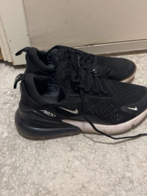 Nike Air Max  svarta sneakers - Svarta Nike Air Max 270 sneakers med vit sula och synlig Air-enhet i hälen. Ovandelen är i mesh för bra ventilation och har små vita Nike-loggor på sidan och framtill. Skorna har snörning och en sportig, modern look.