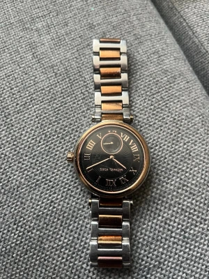 Michael Kors klocka i roséguld och silver - Snygg klocka från Michael Kors med rund svart urtavla, romerska siffror och detaljer i roséguld. Länken är tvåfärgad i roséguld och silver, vilket ger en elegant look. Klockan har en klassisk design med metallarmband och stilrena detaljer.
