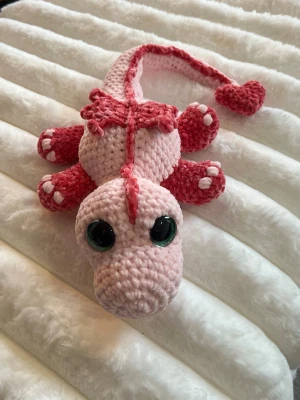 Urgullig rosa drake - Detta är en urgullig ljus rosa drake med mörkrosa detaljer, virkat med mjukt garn från Hobbii som heter Baby Snuggle och mjukt garn från Rusta som heter Klara🩷💗💕 Den har hårda gröna ögon som inte går att ta av, sitter som bergen💚✨ Den är cirka 60 cm lång när man sträcker ut svansen✨