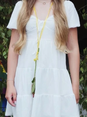 Vit kortklänning med puffärmar - Söt vit kortklänning med puffärmar och knytning framtill. Klänningen har en luftig och lätt design med volangdetaljer och är perfekt för varma dagar. Materialet känns mjukt och behagligt mot huden. Passformen är normal och klänningen har en feminin och ungdomlig stil. använd endast en gång.