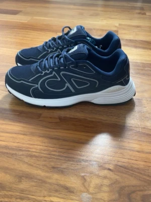 Dior B30 - Snygga mörkblå sneakers med vita detaljer och vit sula. Skorna har en sportig design med mesh och syntetmaterial, samt klassiska snörningar. Perfekta för dig som gillar stilrena och bekväma sneakers.
