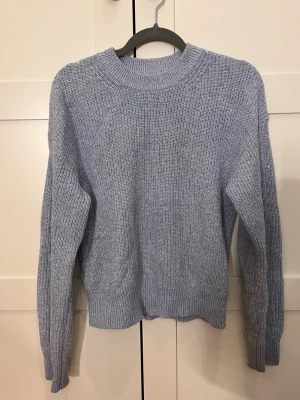 Ljusblå stickad tröja - En enkel och stilren ljusblå stickad tröja med rund halsringning och långa ärmar. Tröjan har ribbade muddar vid ärmslut och nederkant, vilket ger en snygg passform. Perfekt att matcha med jeans eller kjol för en avslappnad look. Fint skick men använd. 