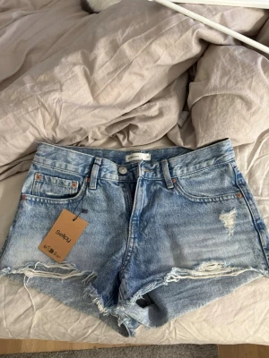 Blå jeansshorts från Gina Tricot - Säljer ett par ljusblå jeansshorts från Gina Tricot med slitna detaljer och råa kanter. Klassisk femficksmodell med knapp och dragkedja. Pris kan diskuteras 