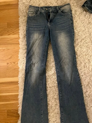 Blå bootcut jeans med dekorerade fickor - Säljer ett par blå bootcut jeans med snygg slitning framtill och bak. Har ba använts 1gång. Jeansen har två bakfickor med dekorativa sömmar och knappar, och normal midja. 