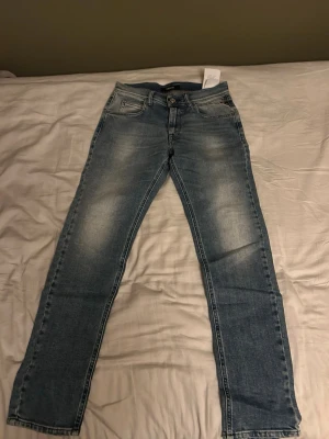 Blå jeans från replay - Säljer ett par klassiska blå jeans från replay med raka ben och snygg slitning framtill. Jeansen har fem fickor, normal midja och är gjorda i ett tåligt denimtyg. Perfekta för en avslappnad och stilren look. Storlek 12y men passar dig runt 160-165 köpta på kidsbrandstore