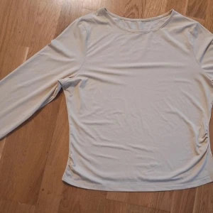 Beige långärmad topp - Säljer en enkel och stilren beige långärmad topp med rund hals. Toppen har en mjuk och stretchig passform som sitter snyggt på kroppen. Perfekt att matcha med jeans eller kjol för en clean look.