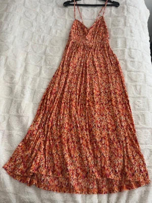 Blommig långklänning med smala axelband,XXL - Långklänning med smala axelband och v-ringning. Klänningen har ett färgstarkt blommigt mönster i orange, rött, rosa och vitt. Luftigt fall och markerad midja, perfekt för varma dagar. Materialet känns lätt och mjukt mot huden.