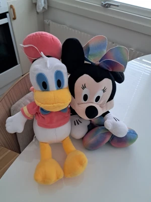 Mimmi Pigg & Kalle Anka gosedjur - Två stora mjukisdjur söker nytt hem! Här har vi inte Musse – utan Mimmi Pigg i en fantastisk regnbågsfärgad klänning med matchande rosett, redo för fest när som helst! Och bredvid henne står Kalle Anka i röd tröja och blå fluga – alltid lika stilig (och kanske lite småsur, men på ett gulligt sätt. De är ca 50 cm höga, färgglada, mjuka och fulla av personlighet. Perfekta som dekoration i barnrummet, som blickfång i soffan eller som trogna kramkompisar under filmkvällen. Tvättade! Priset för båda