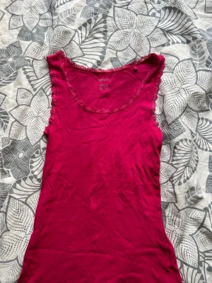 Mörkrosa ribbad linnetopp Esmara - Snygg mörkrosa ribbad linnetopp från Esmara med spetsdetaljer runt halsringning och ärmhål. Perfekt att styla till jeans eller kjol för en trendig look. Tillverkad i mjuk bomullsmix för extra komfort.