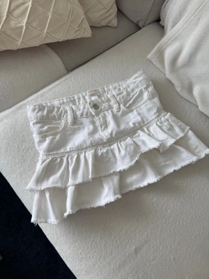 Vit jeanskjol med volang - Vit kort jeanskjol med volang och justerbar midja! Storlek 146 och säljer då den tyvärr är för liten på mig 💗 Prisförslag välkomna 😊 Möjligtvis lite gulnad på vissa ställen i vissa ljus men inget jag tycker märks av alls!! På vissa ställen finns det även små svarta trådar i tyget, det är inte smuts.  Kika gärna in mina andra plagg, vill bli av med så mycket som möjligt 🥂