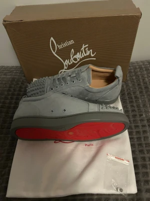 Gråa Christian Louboutin sneakers - Snygga gråa sneakers från Christian Louboutin i mocka med ikoniska röda sulor och coola nitar på tån. Skorna är i storlek 42. Tveka inte om du har några frågor eller funderingar om skorna. Pris kan diskuteras 