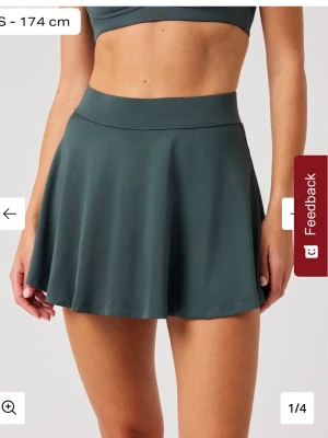 Mörkgrön kort Padelkjol - Snygg mörkgrön padel kjol med hög midja och utsvängd passform. Kjolen är tillverkad i ett stretchigt syntetmaterial som passar perfekt för träning eller tennis. Enkel och stilren design utan mönster eller extra detaljer.