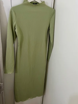 Ljusgrön klänning - En stilren ljusgrön klänning med lång ärm och hög hals. Klänningen har en rak passform och är tillverkad i ett mjukt, stretchigt material som ger en bekväm känsla. Perfekt för dig som gillar minimalistisk stil.