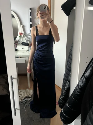 Marinblå balklänning utan band - Elegant mörkblå balklänning utan band. Klänningen har en figurnära passform, slit vid benet framtill och är tillverkad i ett glansigt material, satin. Perfekt för bal. Bara använd en gång.