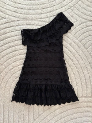 Supergullig svart spetsklänning med volang  - En super gullig och unik svart spetsklänning med volanger från Dry lake. Med spets, volangdetaljer och oneshoulder- modell.  Den är i nyskick, aldrig använd 🩷