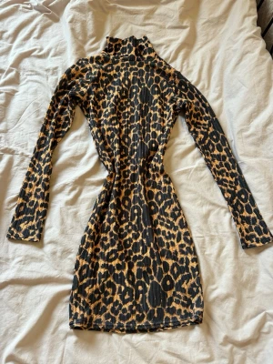 Leopardmönstrad ribbad kortklänning - Säljer en leopardmönstrad ribbad kortklänning med polokrage och långa ärmar. Klänningen har en tight passform och är i stretchigt material, perfekt för dig som vill sticka ut. Färgerna går i svart och beige med klassiskt leopardmönster.