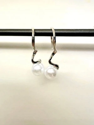 Silvriga örhängen med pärlor - Unika örhängen i 925 sterling silver med en vågig design och vita pärlor. Snyggt minimalistiska och perfekta för dig som gillar stilrena accessoarer med en twist. Märkta med S925 för äkta silver. Knappt använda i väldigt fint skick! Mått 25mm. 