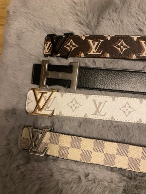Valfri styck - Fyra snygga Louis Vuitton bälten i olika färger och mönster. Ett brunt med klassiskt monogram, ett svart med silverfärgat spänne, ett vitt med monogram och guldfärgat spänne samt ett beige-rutigt med silverfärgat LV-spänne. Perfekta accessoarer för att lyfta din outfit.