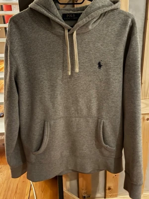 Grå hoodie från Polo Ralph Lauren - Snygg grå hoodie från Polo Ralph Lauren med klassisk huva och vita dragsnören. Storlek S. Mycket bra skick! Kvitto går att lösa!