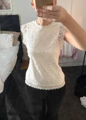 Vit spetsblus med korta ärmar - Säljer en söt vit blus i spets med fina detaljer och korta ärmar. Toppen har rund halsringning och vågig kant nertill samt vid ärmslut. Perfekt att styla med både jeans och kjol.