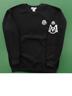 Svart sweatshirt från Zara  - Svart sweatshirt från Moncler med rund halsringning och ribbade muddar. Tröjan har vita och röda logodetaljer på bröstet och ärmen samt en stor vit Moncler-logga på ärmen. Perfekt för en stilren och trendig look.