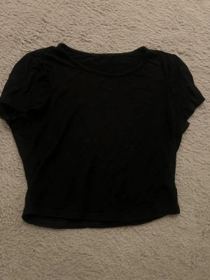 Svart croppad t-shirt - En enkel svart croppad t-shirt med korta ärmar och rund halsringning. Perfekt att matcha med jeans eller kjol för en avslappnad look. Lite stor för mig som brukar ha S