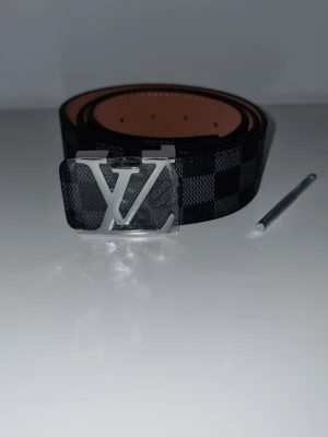 L.V bälte - Snyggt svart rutigt skärp från L.V med stor silverfärgad L.V logga som spänne. Utsidan har klassiskt Damier-mönster och insidan är ljusbrun. Perfekt accessoar för att lyfta din outfit.