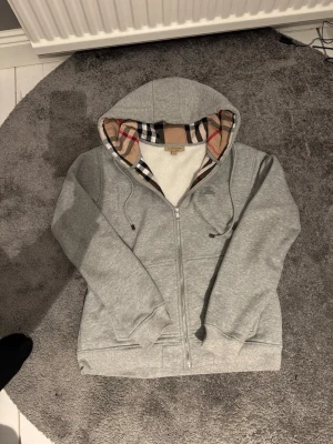 Grå zip hoodie från Burberry - Snygg grå zip hoodie från Burberry, storlek L men skulle Apsolut säga att den passar dig som bär M, priset är inte hugget så kom med bud, gärna snabb affär😁