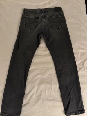 Lee jeans - Säljer ett par svarta jeans från Lee med klassisk femficksdesign och slim fit. Jeansen har tydliga sömmar och en svart patch med Lee-logga bak i midjan. Byxorna är knappt använda och i nyskick, nypris ca 1000kr. Storlek 30/30