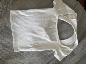 Vit ribbad topp med öppen rygg - Säljer en vit ribbad topp med korta ärmar och snygg öppen rygg. Toppen har en tight passform. Materialet är mjukt och stretchig. Säljer då den har blivit för liten