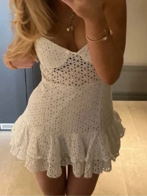 Vit spetsklänning med volang - Söt vit kortklänning med broderad spets och volangkant. Klänningen har smala axelband, v-ringad urringning och är ärmlös. Jag har sytt om den från L till S 