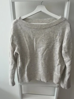 Beige stickad tröja från Gina Tricot - Mysig beige stickad tröja från Gina Tricot med bred ribbad halsringning och ribbade muddar vid ärmslut och nederkant. Tröjan har en avslappnad passform och materialet är mjukt och fluffigt, vilket gör den extra skön. Köparen står för eventuell frakt.