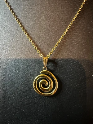 Guldigt halsband med spiralhänge - Snyggt halsband i guldfärgad metall med ett unikt spiralformat hänge. Kedjan är tunn och klassisk, vilket gör att det coola hänget verkligen står ut. Perfekt accessoar för dig som gillar statement-smycken och vill ha något som drar blickarna till sig.